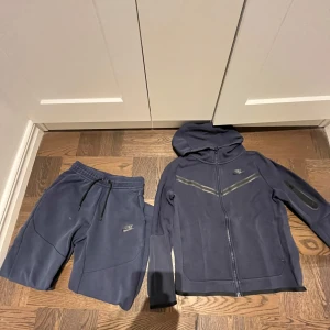 Gamla nike tech i mörkblå - Säljer en mörk blå nike tech dress med dragkedja och huva. Tröjan och byxorna säljs inte längre de är limiterade kvar på marknaden. Tröjan och byxorna har flera fickor och en stor på sidan av tröjan/byxorna  och reflekterande detaljer på bröstet och ärmarna. Perfekt för en ung grab som är vid 147/158 men också ister perfekt 162 längden. De är storlek L men i barn.