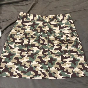 Camouflage kjol från Zara - Snygg kortkjol i camouflage från Zara med praktiska fickor framtill. Kjolen har en dragkedja bak och är perfekt för en cool och avslappnad stil. Tillverkad i ett slitstarkt material som ger en skön passform.