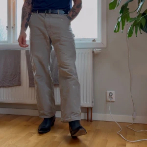 Carhartt byxor  - Snygga beige cargobyxor med praktiska fickor och bälte. Perfekta för en avslappnad stil. Byxorna har en normal passform och är tillverkade i slitstarkt material. Färg och lim finns på byxorna.