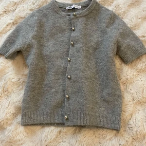 Grå kofta från Zara - Säljer en grå kofta från Zara med korta ärmar och knappar framtill. Perfekt för lager-på-lager och passar till många olika outfits. Koftan är mjuk och bekväm🤍🤍 har bara änvänt få tal gånger.