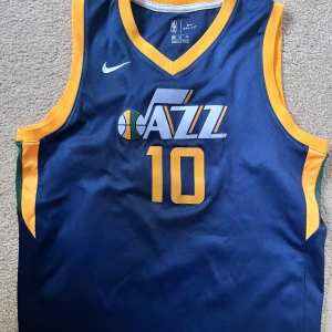 Blå basketlinne från Nike - Säljer en blå basketlinne från Nike med gult och vitt tryck. Den har nummer 10 och texten 'Jazz' på framsidan samt 'Conley' på baksidan. Perfekt för basketfans! 🏀