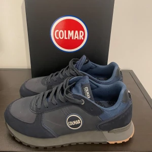 Mörkblå sneakers från Colmar - Snygga mörkblå sneakers från Colmar med snörning och en stilren design. Skorna har en robust sula och är tillverkade i en kombination av mocka och syntetmaterial. Perfekta för en casual look. Skriv om ni har funderingar och priset är inte hugget i sten!