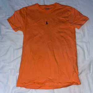 Orange t-shirt från Ralph Lauren - Säljer en unik och snygg orange t-shirt från Ralph Lauren med en liten blå broderad Ralph Lauren logga på bröstet. T-shirten har en riktigt bra passform och är kortärmad, perfekt T-shirt nu till sommaren. Skick: 10/10, pris inte hugget i sten. Har du några andra funderingar så kan du höra av dig i dm😊🙌 // DeLuxe Resells