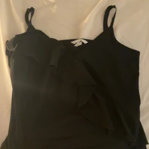 Svart ärmlös topp med volangdetalj - Snygg svart ärmlös topp med volangdetalj framtill. 