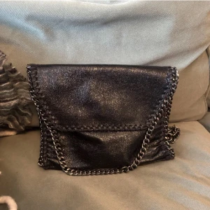 Svart axelväska med kedjedetaljer - Snygg svart axelväska med kedjedetaljer och flätade kanter. Nyskick