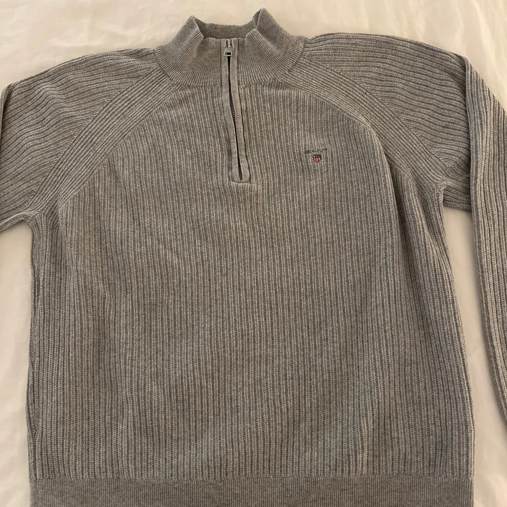 Säljer en stilren grå stickad tröja från Gant med dragkedja vid halsen. Tröjan har långa ärmar och en liten broderad logotyp på bröstet. Perfekt för kyligare dagar! Storlek 158/164. Skicka till mig om du har några frågor.. Neuletakit & Villapaidat.
