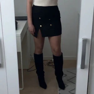 Svart kortkjol med knappar - Ursnygg svart kjol med guldknappar. Aldrig använd 🖤