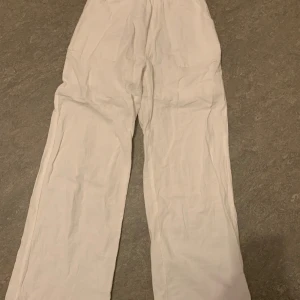 Vita linnebyxor med elastisk midja - Snygga vita linnebyxor med elastisk midja och knappdetalj. Byxorna har en loose passform och raka ben, vilket ger en avslappnad look. Perfekta för varma sommardagar.