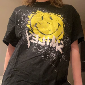 Smiley t-shirt  - Cool oversized svart t-shirt från H&M med ett stort gult smileytryck och texten 'Smiley' i vitt. Perfekt för en avslappnad stil med en touch av humor. Passar bra till både jeans och kjol.