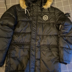 Svart dunjacka från Just Hype - Säljer en svart dunjacka från Just Hype med pälskantad huva och dragkedja. Oanvänd, endast provad.