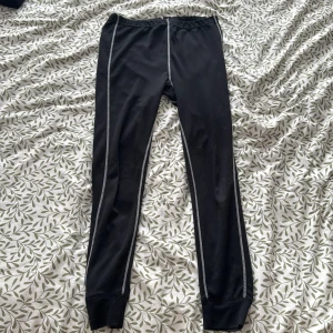 Svarta leggings med kontrastsömmar - svarta leggings med vita kontrastsömmar längs benen. Perfekta för en sportig look eller avslappnad stil. Elastisk midja för bekväm passform.