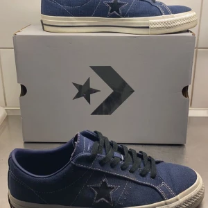 Blå sneakers från Converse - Snygga blå sneakers från Converse med stjärndetalj på sidan. Skorna har svarta snören och en vit sula som ger en klassisk look. Perfekta för en avslappnad stil. Bara att höra av sig ifall du har frågor eller funderingar:)