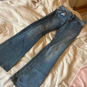 Blå jeans från Gina Tricot - Snygga blå jeans från Gina Tricot i storlek 164. De har en klassisk femficksdesign med dragkedja och knapp framtill. Perfekta för en avslappnad stil med en bootcut passform.