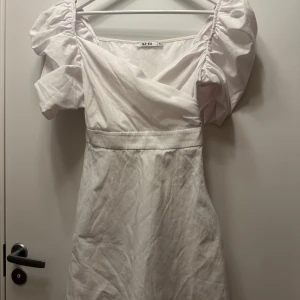 Vit klänning från NA-KD - Säljer en söt vit klänning från NA-KD med puffiga kortärmar och omlott-design. Perfekt för sommarens alla tillfällen. Klänningen har en smickrande passform och är gjord i ett lätt material 💓