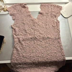 Lila/rosa spets topp - Säljer en söt rosa spetsblus med korta ärmar och vackra vågiga kanter. Perfekt för en romantisk look. Blusen har ett detaljerat blommönster och är gjord i ett mjukt spetsmaterial. Köpt på plick.❤️Storlek S passar som M