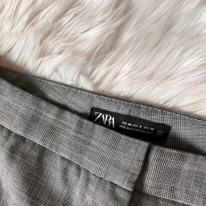 Grå rutig kostymbyxa från Zara - Snygga grå kostymbyxor med ett diskret rutmönster. Byxorna har en mid-waist passform och raka ben (obs fejk fickor bak!)🩶