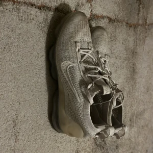 Grå Nike Vapormax sneakers - Snygga grå Nike Vapormax sneakers med stickad ovandel och synlig luftdämpning i sulan. Skorna har snörning och en modern design som passar perfekt för en sportig look. Storlek 39 ny pris 2500 säljer för 550
