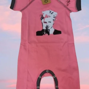 Rosa kortärmad babyromper med ikoniskt tryck (Storlek 74-80) - Låt din lilla rockstjärna sticka ut i denna unika rosa babyromper med ett ikoniskt ansiktstryck. Med kontrasterande mörkgrå detaljer, praktiska tryckknappar och en cool design är denna romper både bekväm och stilfull för de minsta. Perfekt för vardagsbruk eller som en rolig present!  Specifikation 	Kategori: Barnkläder (Babyromper) 	Färg: Rosa med mörkgrå detaljer 	Design: Ikoniskt ansiktstryck 	Ärm: Kortärmad 	Storlek: 74-80 (ca 6-12 månader) 	Detaljer: Tryckknappar för enkel på- och avklädning