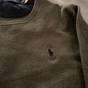 Olivgrön tröja från Ralph Lauren - Säljer en stilren olivgrön tröja från Ralph Lauren med rund halsringning och broderad logotyp på bröstet. Perfekt för en avslappnad och snygg look.