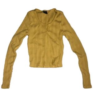 Gul ribbad crop top från Gina Tricot - Säljer en snygg gul ribbad tröja från Gina Tricot. Tröjan har en v-ringad design och långa ärmar. 