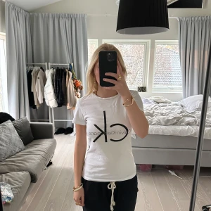 Vit t-shirt från Calvin Klein - Säljer en klassisk vit t-shirt från Calvin Klein i storlek S. Den har en stor 'ck' logga på framsidan och är gjord i mjuk bomull. Perfekt för en avslappnad stil eller som basplagg i garderoben. Kortärmad och i mycket bra skick!