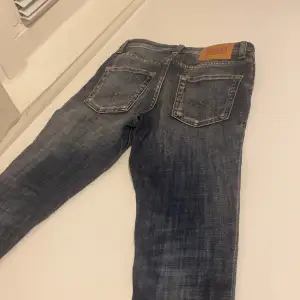 Säljer ett par snygga blå jeans från Jack & Jones i storlek 146. De har en cool slitning på framsidan och klassiska fem fickor. Perfekta för en avslappnad stil. Passar både till vardags och fest!