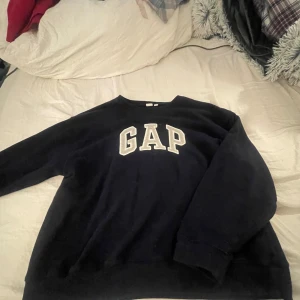 Mörkblå sweatshirt från GAP - Säljer en klassisk mörkblå sweatshirt från GAP i storlek L. Tröjan har en stor GAP-logga på bröstet och är perfekt för en avslappnad stil. Den är i bra skick och passar både höst och vinter. Perfekt för mysiga dagar eller en casual look.