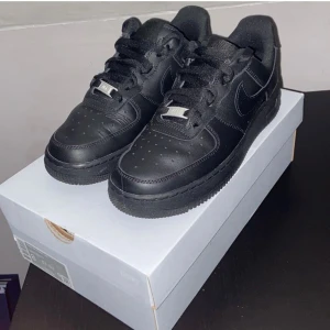 Svarta Nike Air Force 1 '07 - Säljer ett par klassiska svarta Nike Air Force 1 '07. Skorna är i nytt skick och har en stilren design med snörning och en robust sula. Perfekta för både vardag och fest!