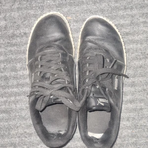 Svarta sneakers från Puma - Säljer ett par svarta Puma sneakers i acceptabelt skick. Skorna har en vit sula och klassisk snörning. Perfekta för vardagsbruk men har lite slitage invändigt. Passar bra till både jeans och shorts.