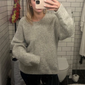 Grå stickad tröja - Mysig grå stickad tröja perfekt för kyliga dagar. Den har en avslappnad passform med långa ärmar och ribbade kanter. Perfekt för både höst och vinter, och funkar lika bra till jeans som till en kjol. Superbekväm och stilren! Nypris 800kr, lite stickig 
