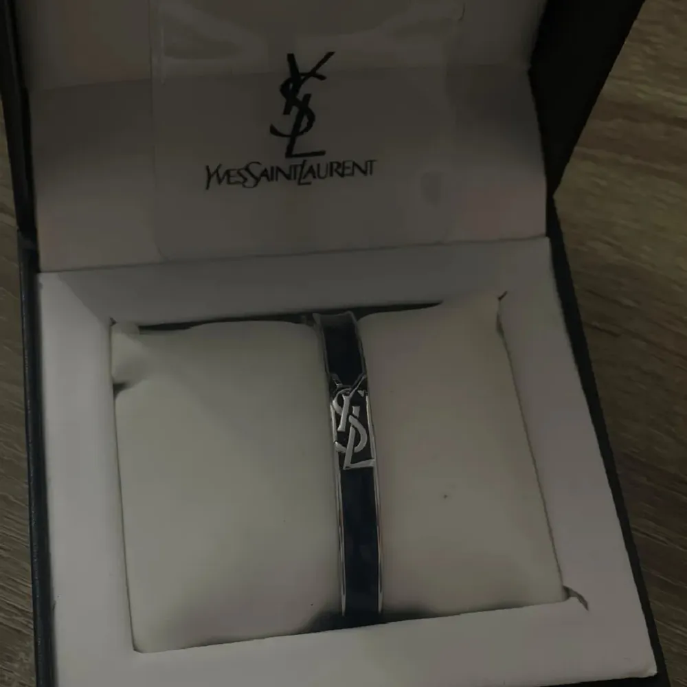 Snyggt och stilrent armband från Yves Saint Laurent i en elegant svart färg. Armbandet har en ikonisk YSL-logga i silver som ger en lyxig touch. Perfekt accessoar för både vardag och fest. Kommer i originalförpackning.. Accessoarer.