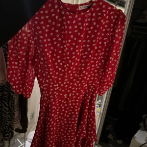Röd blommig klänning från ADOORE - En onanvönd röd klänning från ADOORE med sött blommönster. Den är i nytt skick och har en härlig volangdetalj och kprta armar 