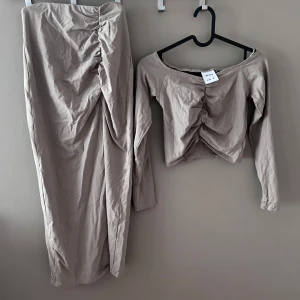 Beige set från Lefties - Säljer ett snyggt beige set från Lefties. Setet består av en långkjol och en långärmad topp, båda med snygg rynkdetalj framtill. Perfekt för både vardag och festliga tillfällen. Materialet känns mjukt och bekvämt. Passa på att köpa detta stilrena set! Kjolen är i xs och har slits