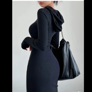 Svart långklänning med huva - Snygg svart långklänning med huva, perfekt för en stilren look. Klänningen är tight och har långa ärmar. Oanvänd. 