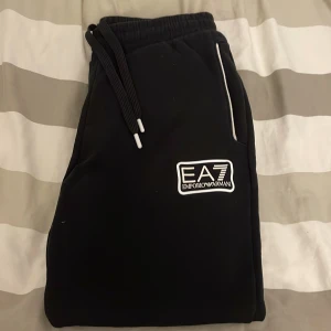 Svarta mjukisbyxor från Emporio Armani - Säljer ett par svarta mjukisbyxor från Emporio Armani i storlek S. Byxorna har en elastisk midja med snörning och en snygg logga på benet. Perfekta för en avslappnad stil eller träning. De är i mycket bra skick och superbekväma!