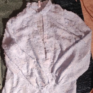 Ljusblå spetsblus / skjorta  - Säljer en elegant ljusblå blus/skjorta med vacker spetsdetalj. Blusen har långa ärmar och en stilren design som passar perfekt för festliga tillfällen. Materialet känns lyxigt och ger en romantisk känsla. Perfekt för vår och sommar! Den är genomskinlig och tunn.