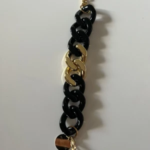 Svart och guld armband by Jolima - Snyggt armband med stora länkar i svart och guld. Perfekt för att ge en elegant touch till din outfit. Armbandet har en modern design och passar både till vardags och fest. Ett måste för smyckesälskare!