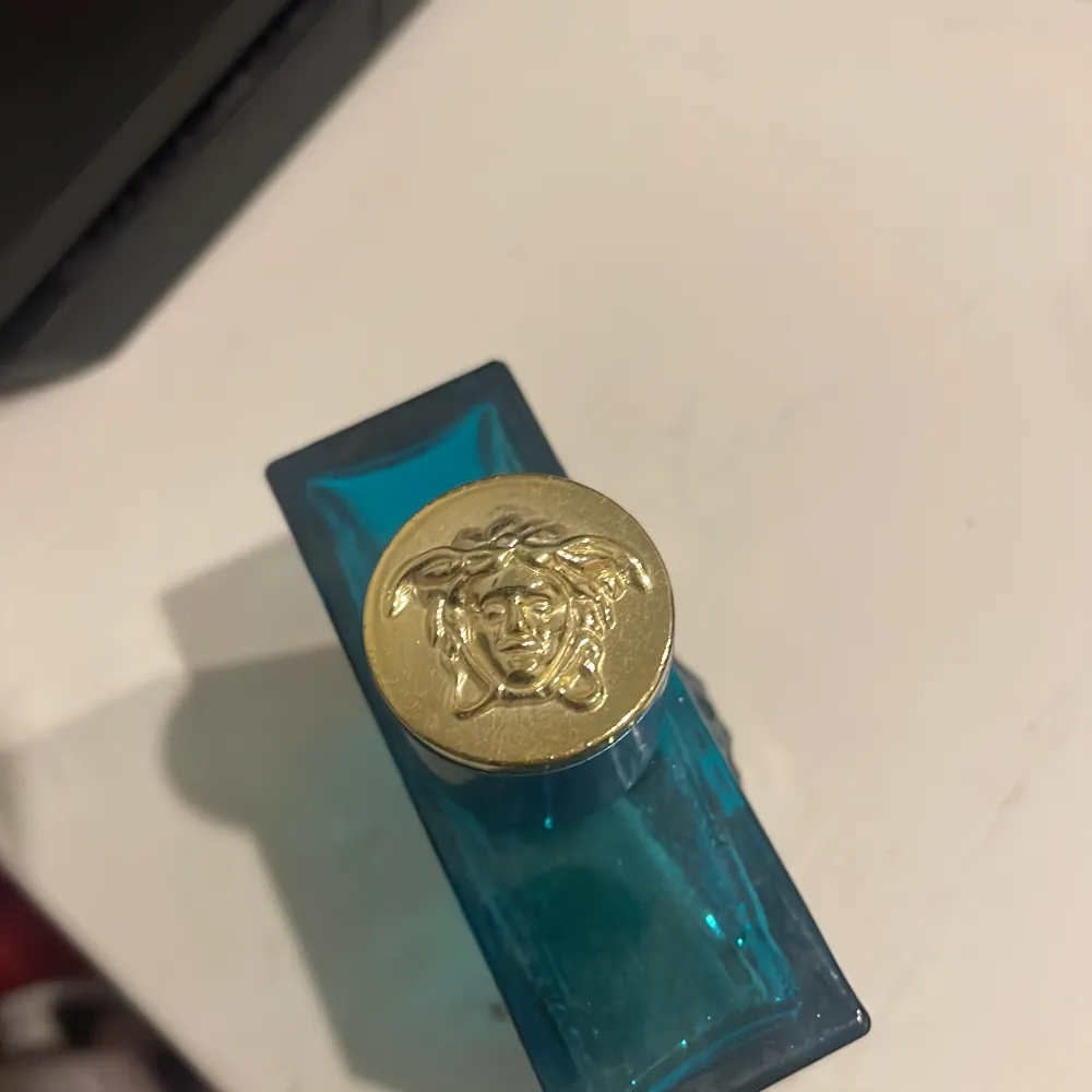 Säljer en flaska Versace Eros Eau de Parfum, 100 ml. Flaskan är i en snygg turkos färg med ett elegant mönster och har en guldig kork med Medusa-loggan. Perfekt för den som vill ha en fräsch och maskulin doft. Flaskan är nästan full och i bra skick. Passa på att köpa denna lyxiga parfym till ett bra pris!. Parfym.