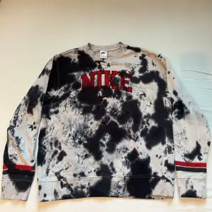 Säljer en cool tie-dye sweatshirt från Nike i svart och grått med röd broderad logga på bröstet. Tröjan har långa ärmar och är perfekt för en avslappnad stil. Den är i mycket bra skick och passar perfekt för höst och vår.