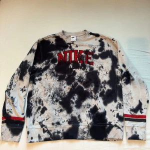 Nike tie-dye sweatshirt - Säljer en cool tie-dye sweatshirt från Nike i svart och grått med röd broderad logga på bröstet. Tröjan har långa ärmar och är perfekt för en avslappnad stil. Den är i mycket bra skick och passar perfekt för höst och vår.