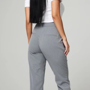 Grå kostymbyxor - Säljer ett par stilrena grå kostymbyxor i storlek 46. De har en hög midja och en rak passform som ger en klassisk look. Perfekta för både kontoret och mer formella tillfällen. Byxorna är i nytt skick och har en diskret dragkedja framtill.