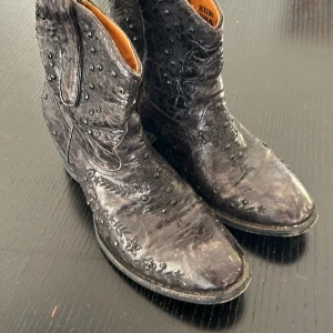 Svarta boots med nitar - Säljer ett par coola svarta mexicana  boots i skinn med strass och dragkedja på sidan. De har en unik textur och är perfekta för höst och vinter. Storlek dam 38. Passar både till vardags och fest!