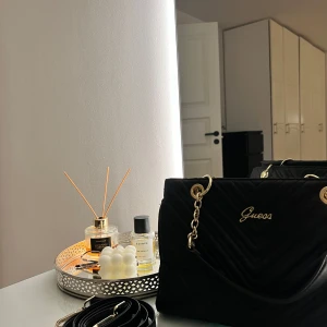 Svart axelväska från Guess - Snygg svart axelväska från Guess i mycket bra skick. Väskan har guldfärgade detaljer och en quiltad design. Insidan är rymlig med flera fack och dragkedja för säker förvaring. Köpt den typ i 2020 för 1240 kr, priser kan diskutera. Tar emot frakt💞