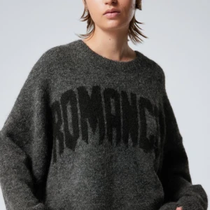 Grå ulltröja med text - Mysig och oversized grå tröja med texten 'ROMANCE' i svart på framsidan. Perfekt för kalla dagar med sin varma ullblandning. Tröjan har långa ärmar och en avslappnad passform som ger en cool och bekväm stil.
