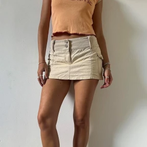 Beige minikjol i cargotyg - Supersnygg och skön beige minikjol! Sitter lowrise, perfekt m en enkel tshirt eller linne i sommar! Midjan är 37 cm platt och längden är 31 cm, jag är 176 cm och tkr att den sitter snyggt!