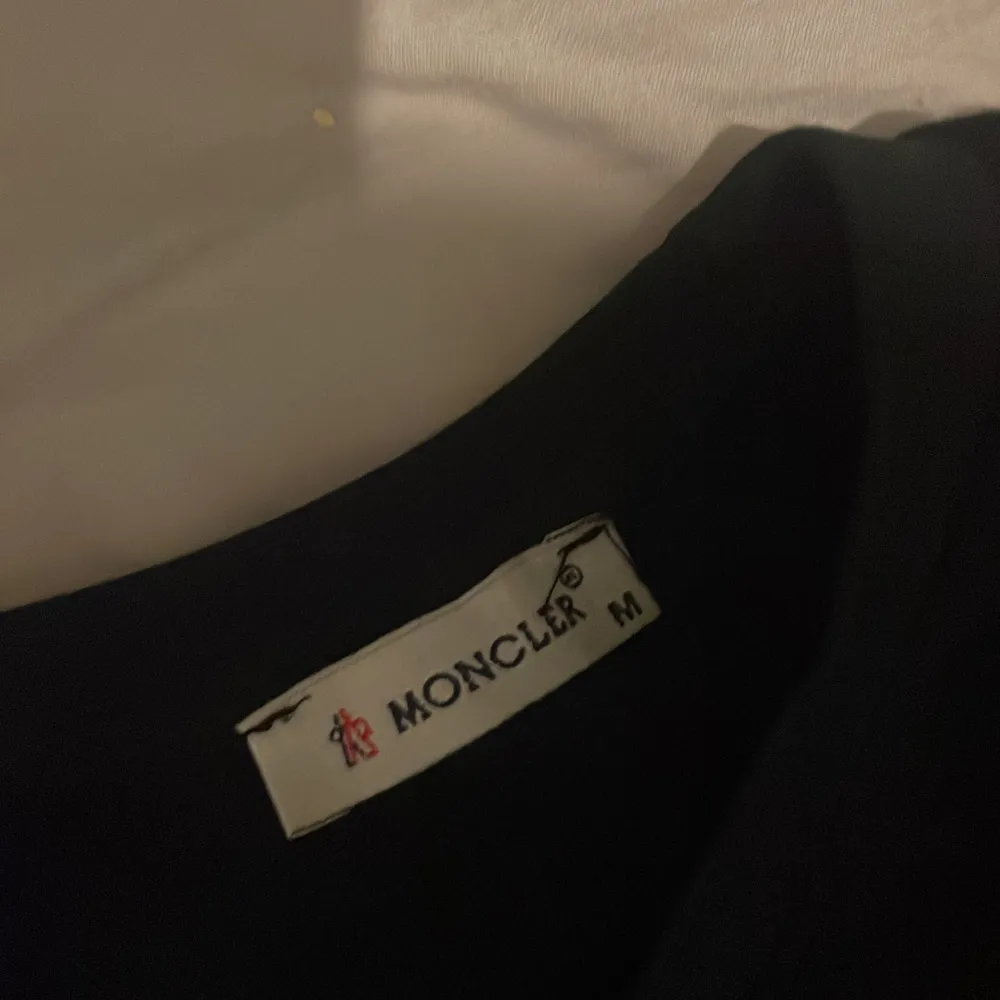 Säljer en stilren svart t-shirt från Moncler i storlek M. Den har en diskret logga på bröstet och är tillverkad i mjukt material för en bekväm passform. Perfekt för både vardag och fest!. T-shirts.