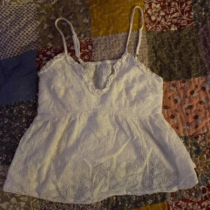 Vit broderad linne - Säljer favorit linnet pågrund av att den är för liten. Det söt vit linne med broderade blommor och smala axelband. Perfekt för sommardagar! Den har en lätt och luftig passform med volangdetaljer vid fållen. Passar bra till både jeans och kjol.