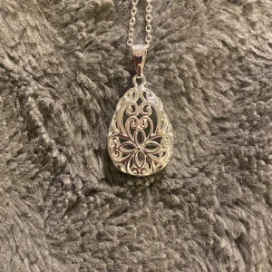 Silver halsband med dekorativt hänge - Elegant silverfärgat halsband med ett detaljerat, droppformat hänge. Hänget har ett vackert utskuret mönster som ger en stilren och sofistikerad look. Kedjan är tunn och smidig med ett enkelt lås för säker användning. Silver 925. Helt ny 