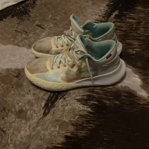 Kyrie irving basketskor - Säljer ett par basketskor med snörning och en sportig design. Skorna har en vit sula och detaljer i mesh för extra ventilation. Perfekta för träning eller en aktiv vardag.