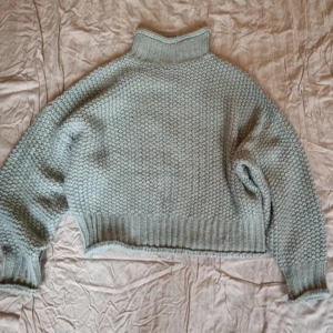 Dimblå stickad polotröja - Mysig dimblå stickad polotröja med hög krage och ribbade detaljer vid ärmslut och nederkant. Perfekt för kyliga dagar och ger en stilren look. Passar bra till jeans eller kjol för en avslappnad stil.